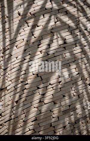 Vertical shot of small off-white marble stone strips stacked diagonally, featuring a strong shadow pattern cast across the surface by natural sunlight Stock Photo