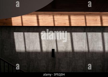 Indoor architectural perspective featuring a dark grey tiled wall illuminated by a geometric beam of sunlight and window frame shadows coming from abo Stock Photo