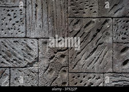 Detailed view of a natural dark grey volcanic basalt stone wall comprised of rectangular blocks with varied surface treatments, including hand-carved Stock Photo