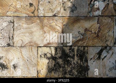 Full frame texture background of a outdoor sandstone block wall featuring natural swirl veining, golden brown hues, weathered surface erosion. Stock Photo