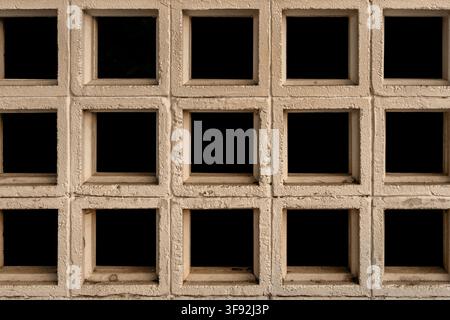 Frontal close-up view of a beige painted breeze block decorative wall showing a grid of square ventilation openings. The repetitive geometric grid. Stock Photo