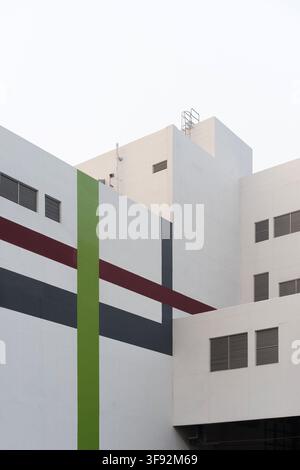 Low angle abstract architectural view of a white multi-story modern building facade decorated with green, maroon, and dark grey geometric accent strip Stock Photo