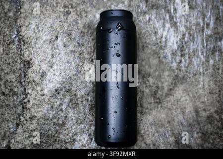 A Sleek Black Insulated Tumbler Covered in Water Droplets Resting on a Wet Stone Surface Stock Photo