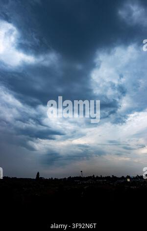 storm clouds gather over a distant low skyline at dusk, creating a dramatic moody sky before an approaching thunderstorm Stock Photo