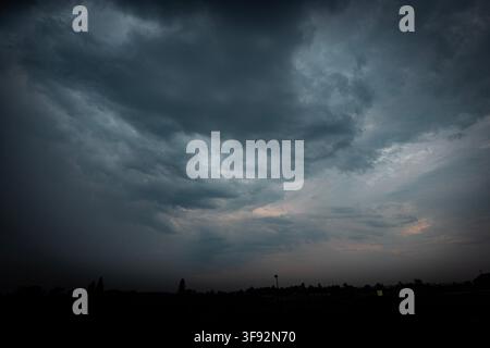 storm clouds gather over a distant low skyline at dusk, creating a dramatic moody sky before an approaching thunderstorm Stock Photo