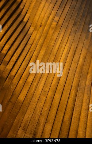 Abstract close-up of a warm golden ridged surface with repeating parallel lines and diagonal perspective, creating a rich textured background Stock Photo