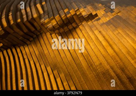 Abstract close-up of a warm golden ridged surface with repeating parallel lines and diagonal perspective, creating a rich textured background Stock Photo
