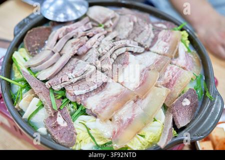 Korean style sukyuk boiled beef platter with various meat cuts and offal served over fresh green vegetables in a warm broth pot. Stock Photo