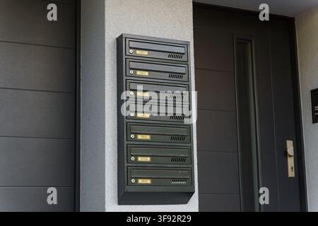 Vertical bank of metallic mailboxes mounted on a speckled grey wall next to a modern dark grey door in an apartment building entrance, postal delivery and secure mail collection Stock Photo