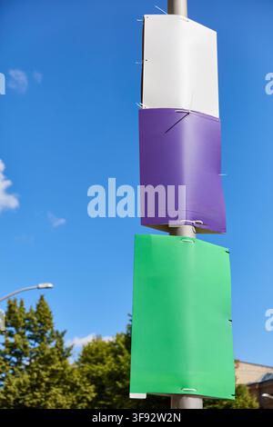 Three completely blank election posters—white, purple, and green—mounted one above the other on a lamppost against a blue Berlin sky. The unprinted su Stock Photo