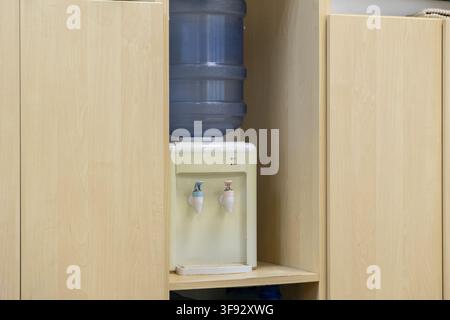 Desktop water dispenser placed on a wooden shelf, offering convenient access to drinking liquid for employees, emphasizing hydration and health in a c Stock Photo