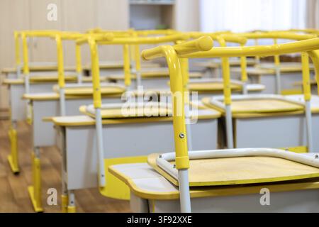 An empty classroom featuring rows of wooden desks with chairs stacked upside down, capturing a serene academic atmosphere waiting for students during Stock Photo