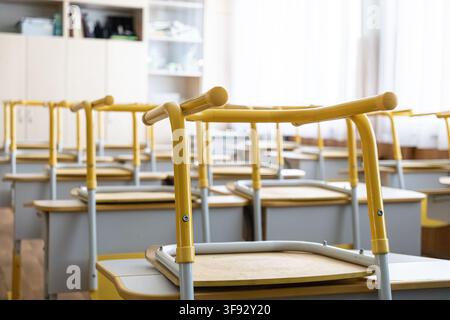 Rows of wooden desks with upturned chairs in a quiet classroom during summer holidays, representing academic downtime, school recess, or the peaceful Stock Photo
