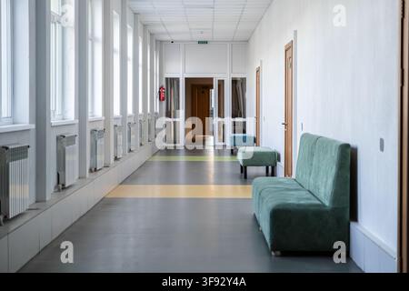 Quiet institutional hallway featuring soft green furniture and sunlight streaming through side windows, reflecting a calm atmosphere in a clinical or Stock Photo