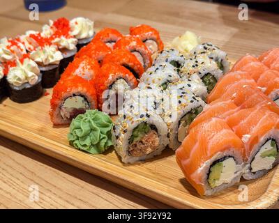 Appetizing platter of various sushi rolls featuring salmon, cream cheese, and spicy fish roe on a wooden serving board to highlight healthy gourmet fo Stock Photo