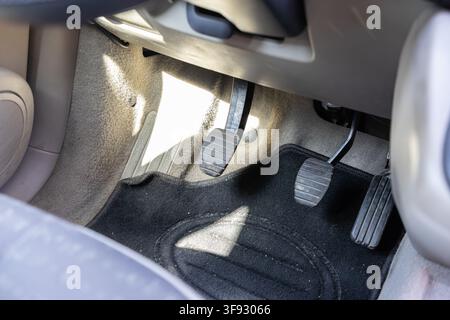 Close up of black rubber foot pedals in a manual transmission car cockpit featuring clutch brake and gas controls under a steering column to illustrat Stock Photo
