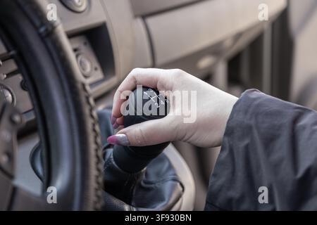 Driver hand gripping the manual transmission gear lever inside a car cabin, conveying focus and mechanical interaction, highlighting the engagement in Stock Photo