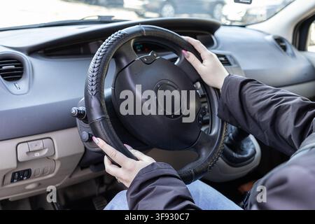 A close view of hands holding a leather steering wheel cover while operating a vehicle, reflecting focus, travel responsibility, and the routine of au Stock Photo