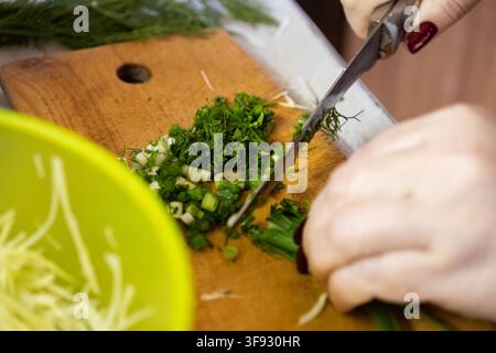 Close up of hands slicing organic herbs on a wooden board, emphasizing culinary preparation and the fresh ingredients used in nutritious home cooking Stock Photo
