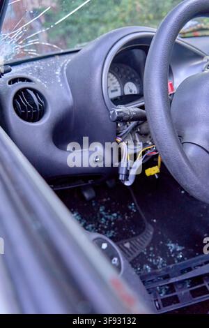 close-up inside a traffic accident or vandalized car with a smashed front windshield, shattered glass shards scattered over the steering wheel Stock Photo