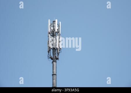A tall steel telecommunications tower equipped with multiple cellular network antennas and transmitters. The mast stands isolated against Stock Photo