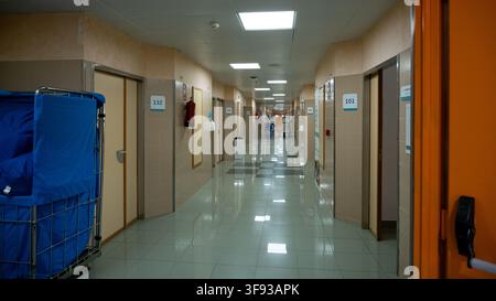 TORREVIEJA, SPAIN - JUNE 23, 2026: An empty hospital corridor displays numbered patient room doors and a metal laundry cart filled with blue linens. Stock Photo