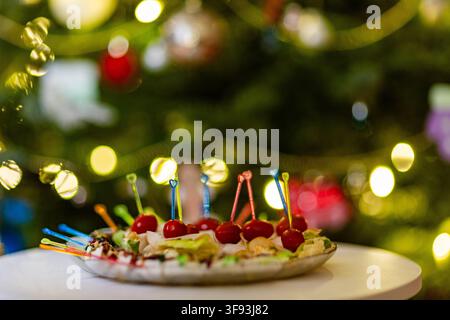 A closeup shot of various colorful appetizers on a plate, set against a festive, blurred background of Christmas tree lights Stock Photo