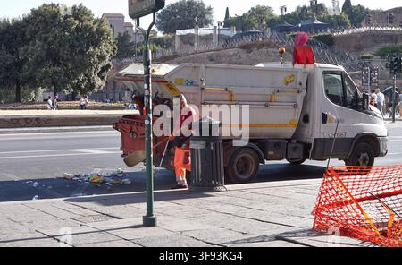 Rome, Italy - June 16, 2026: Sanitation worker in bright orange uniform cleans street near a garbage truck and trash can with historic buildings visib Stock Photo