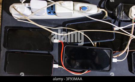 Multiple Smartphones Charging Simultaneously On Power Strips With Tangled Charging Cables Stock Photo