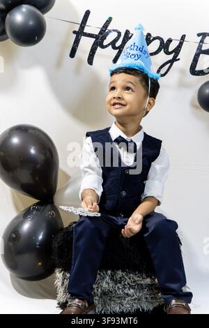 Cute Boy Wearing Party Hat And Formal Clothes At Birthday Celebration playing with bubbles Stock Photo