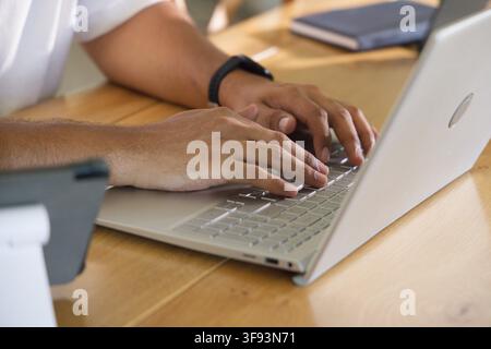 African American man typing on laptop at desk, wearing white shirt, black watch, smartphone nearby Stock Photo