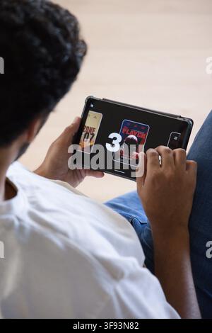 African American man on sofa holding tablet, playing game showing 3 and ZONE 07, copy space Stock Photo