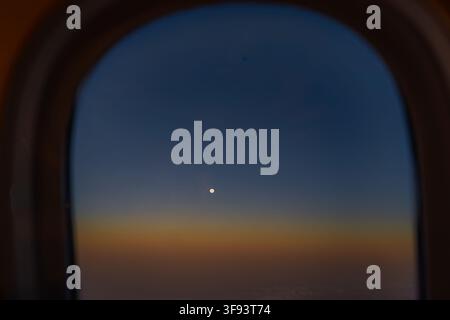 Nighttime view through a commercial aircraft window showing the moon in the dark sky, heavily obscured by reflections from the interior cabin lights. Stock Photo