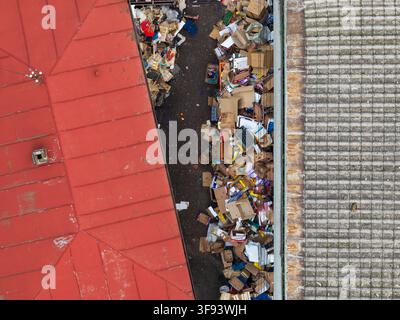 Belgrade, Serbia - 12 November 2025: Aerial view of discarded cardboard boxes and wooden crates piled in a narrow passage between market buildings. Stock Photo