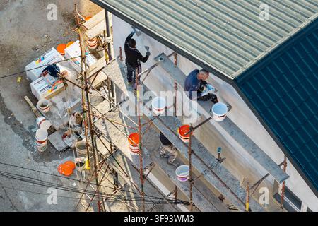 Belgrade, Serbia - 06 November 2025: Aerial view of construction workers on scaffolding applying plaster to a building wall with paint buckets and too Stock Photo