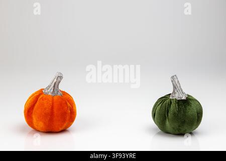 A clean horizontal minimalist shot of two decorative pumpkins in vibrant orange and dark green. The objects are spaced out on a white surface, creatin Stock Photo