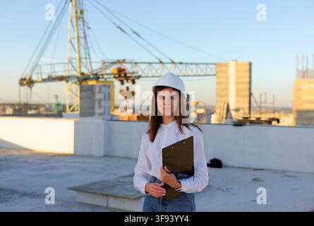 Architect pointing at a blank document on a clipboard, standing on a rooftop with a construction worker, during a site inspection Stock Photo