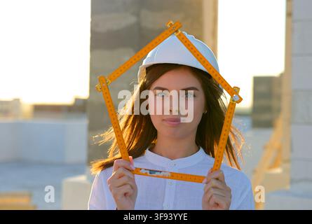 Confident female architect holding a folding ruler while inspecting a building under construction at sunset Stock Photo