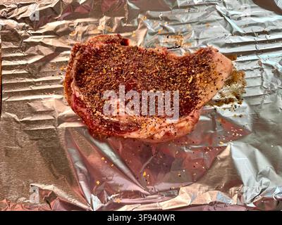 Raw ribeye steak,seasoned & ready to cook on a rack covered with aluminum foil. Kansas,USA. Stock Photo