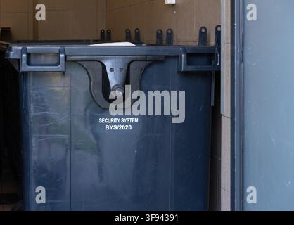 A large wheeled waste container is secured with a locking mechanism at a commercial service area. Stock Photo