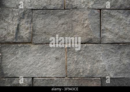 A full frame close up shot of a grey natural stone block wall with rough rectangular textures and dark mortar joints suitable for architecture and int Stock Photo