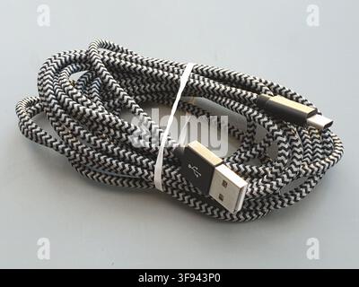 A coiled black and white braided USB cable sits on a grey surface Stock Photo