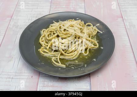 Pesto pasta with grated parmesan cheese served on a dark gray plate over rustic wooden table Stock Photo