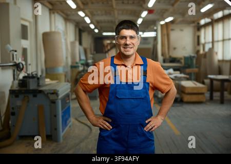 Approachable professional with safety gear standing confidently amid woodworking machinery Stock Photo