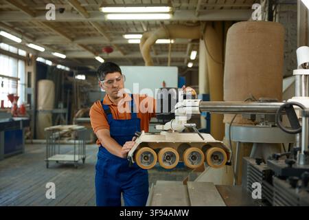 Carpenter adjusting machine settings to ensure consistent thickness and quality of timber Stock Photo