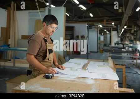 Workman assessing construction drawings in workshop while using measuring instruments and tools Stock Photo
