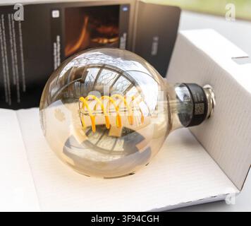 An elegant amber LED light bulb with spiral filament is in a box Stock Photo
