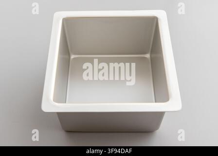 An empty square metal baking pan rests on a plain gray background Stock Photo