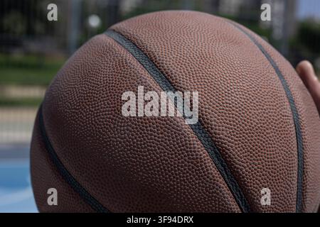 Basketball ball showing detailed texture with a player's hand on an outdoor court Stock Photo