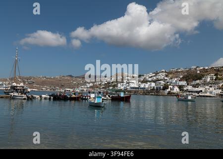 Small boats on flat calm harbour water with the white town on the hill behind, Mykonos, Greece. Stock Photo